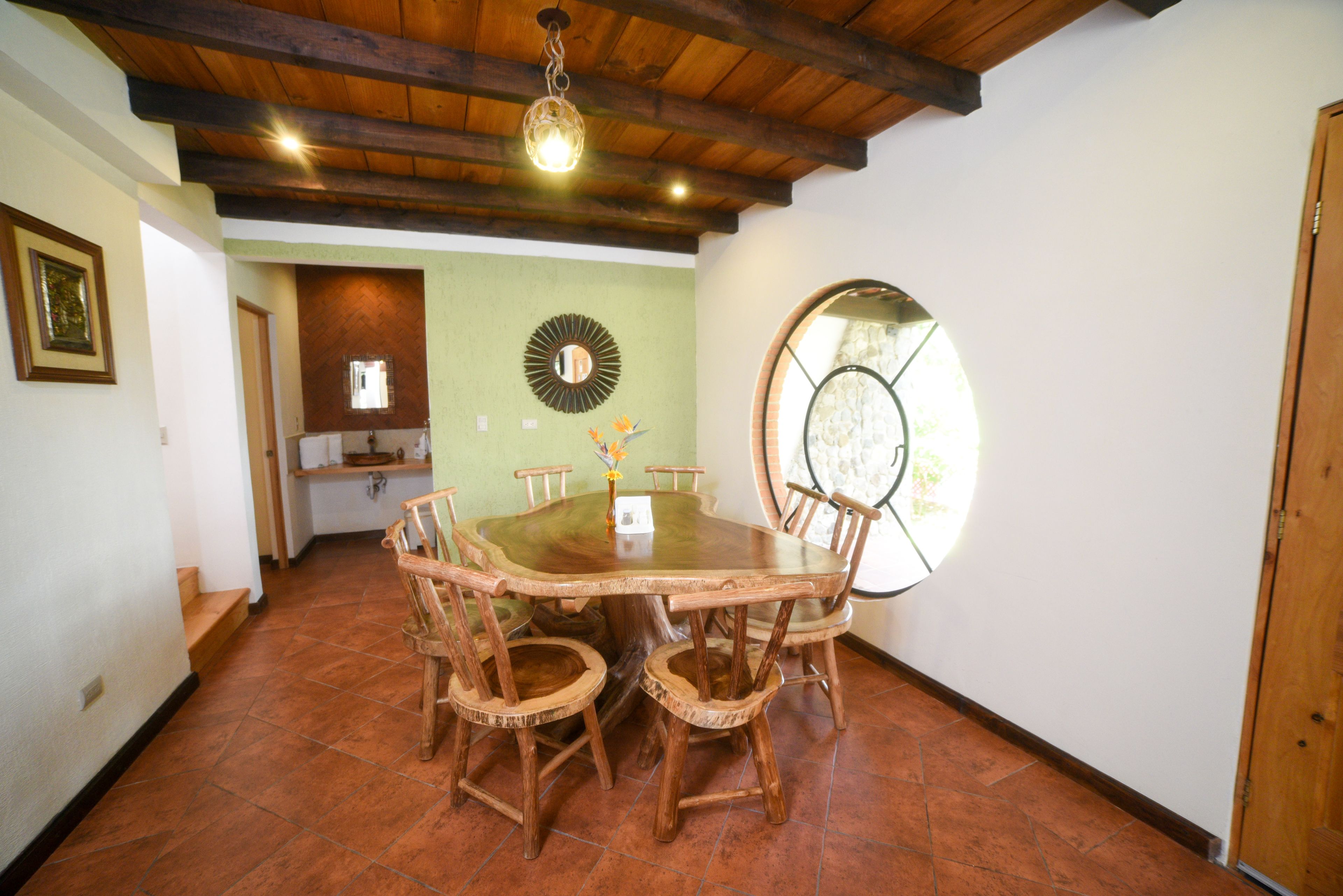 A dining area with a large wooden table surrounded by chairs, a mirror on the wall, and a window with a view.