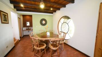 A dining area with a large wooden table surrounded by chairs, a mirror on the wall, and a window with a view.