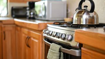 A kitchen with wooden cabinets, a stove, a kettle, and a microwave.