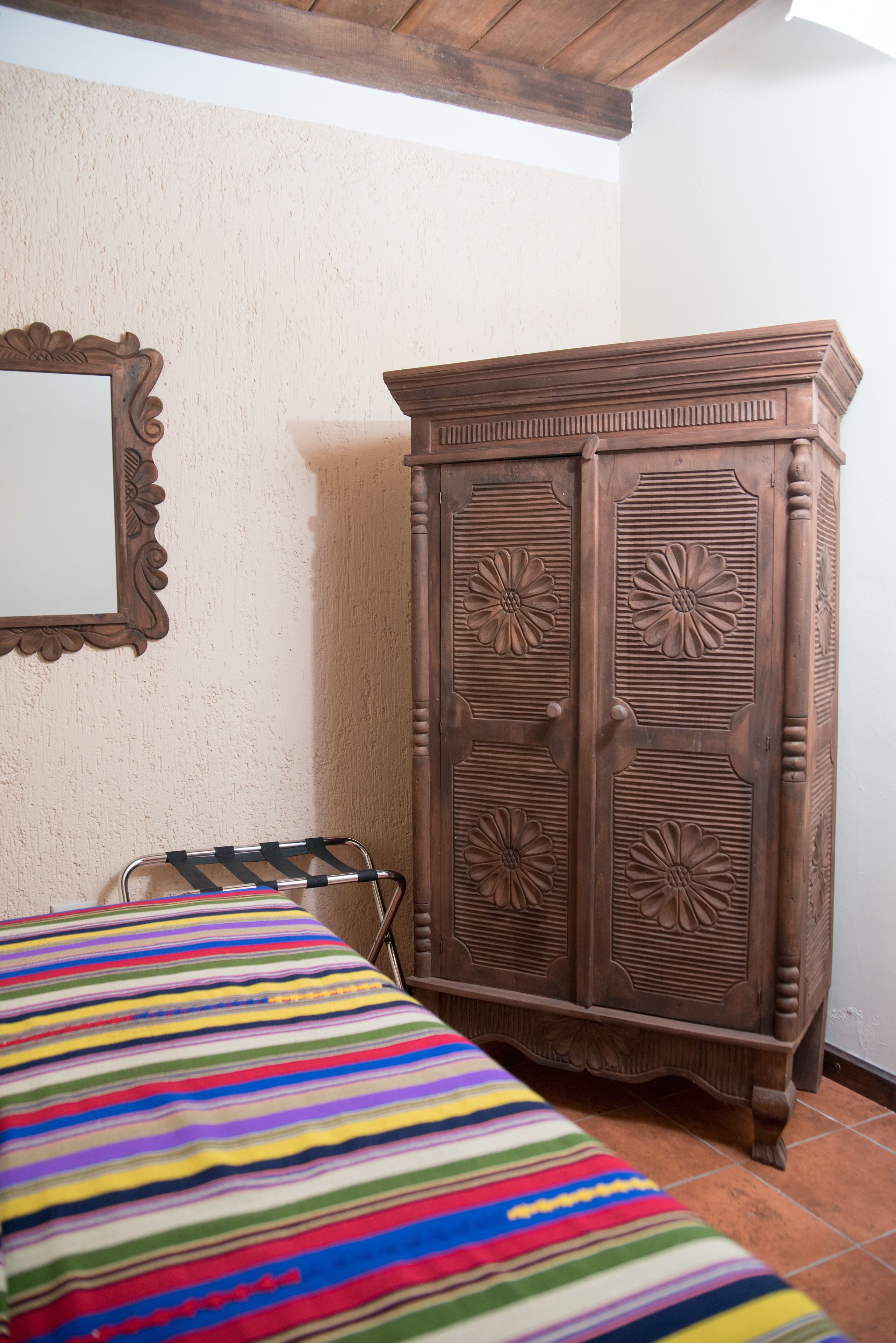 A bedroom with a wooden wardrobe, a striped bedspread, and a mirror on the wall.