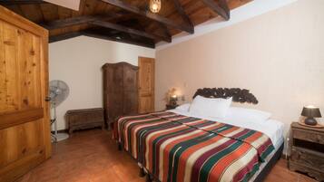 A bedroom with a wooden ceiling, a bed with a striped blanket, a wooden wardrobe, and a nightstand with a lamp.