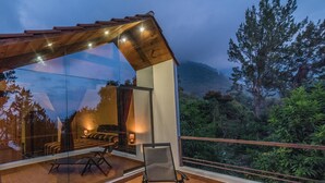 Een modern balkon buiten, met een glazen omheining, een eethoek met tafel en stoelen, en uitzicht op een bergachtig landschap.
