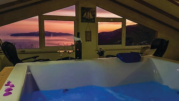 Ein Zimmer mit großem Fenster und Blick auf einen Sonnenuntergang, einer Badewanne und zwei Sesseln.