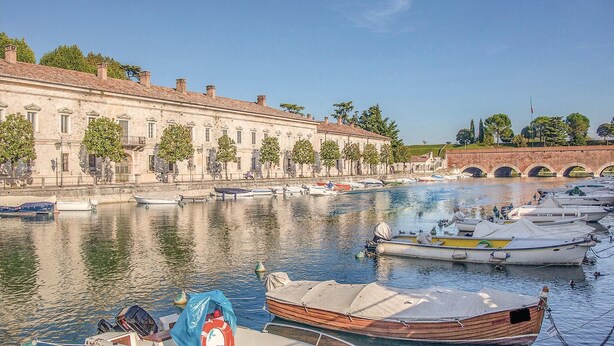 Un canal con barcos amarrados, un edificio histórico con numerosas ventanas y un puente al fondo.
