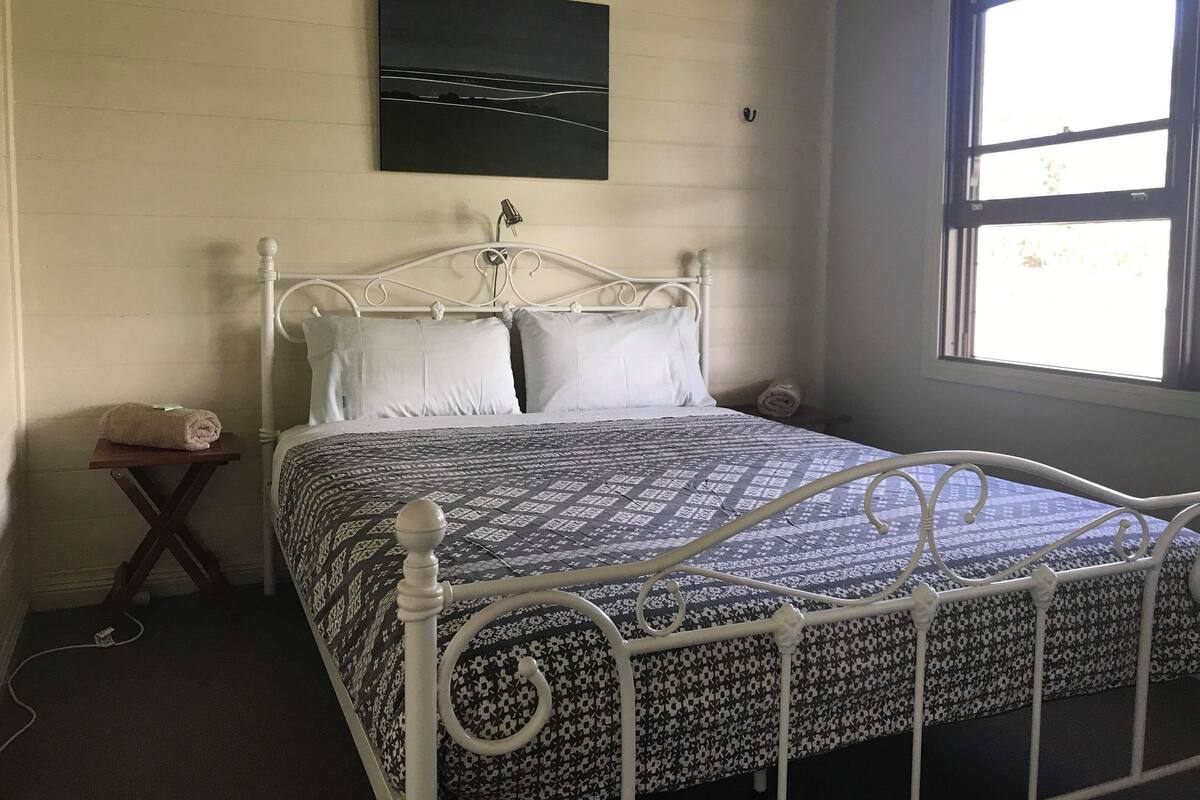 Una cama con colcha estampada, estructura de metal blanco y un cuadro colgado en la pared.