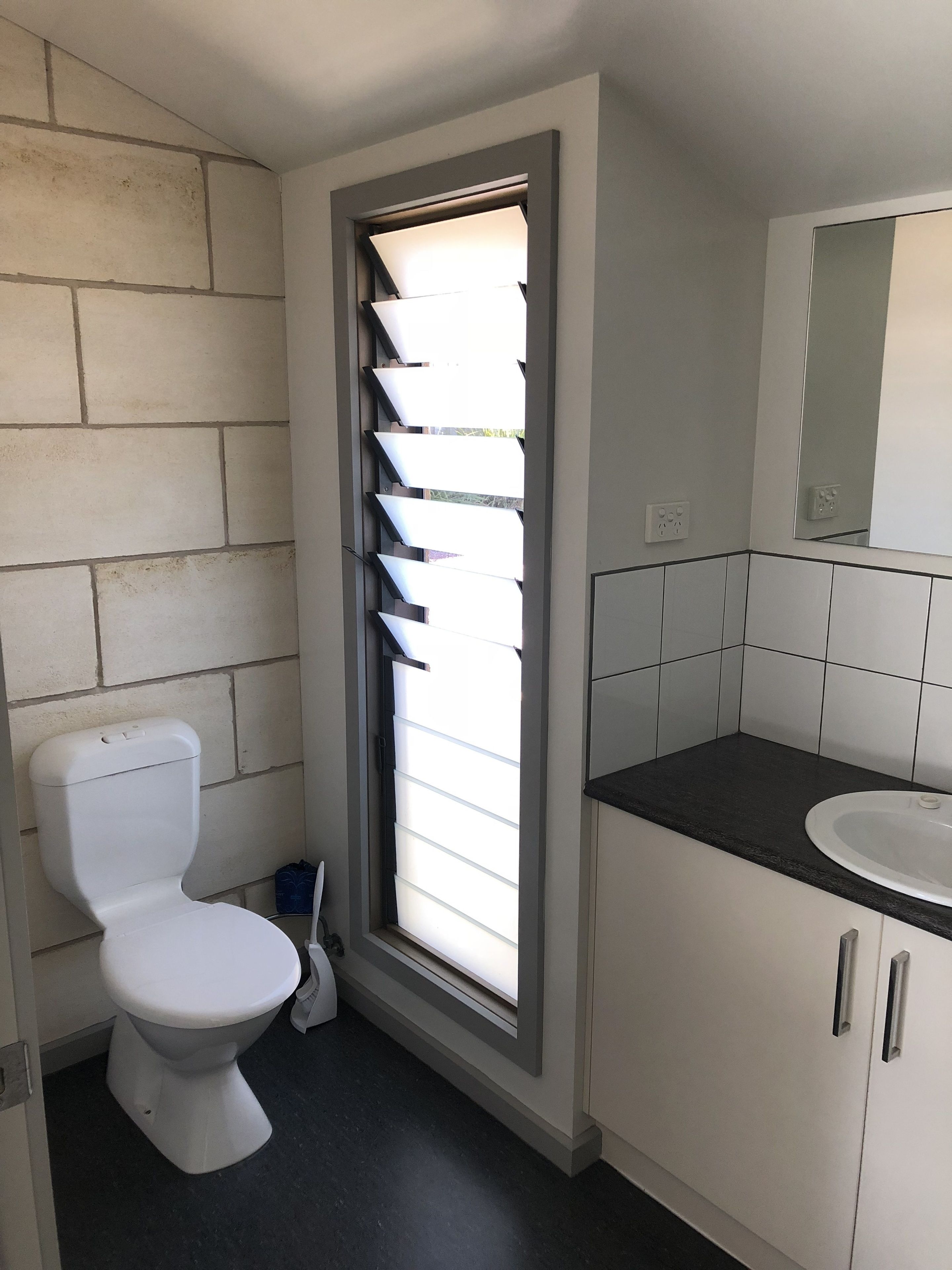 A modern bathroom with a toilet, a window with blinds, a sink, and cabinets.