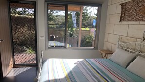 Un dormitorio con cama, ventana, una mesita y una lámpara de pared.