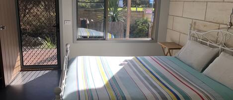 A bedroom with a bed, a window, a small table, and a wall-mounted lamp.