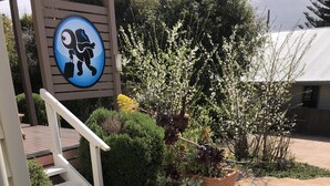 Een tuin met witte bloemen en een bord waarop een figuur een koffer vasthoudt.