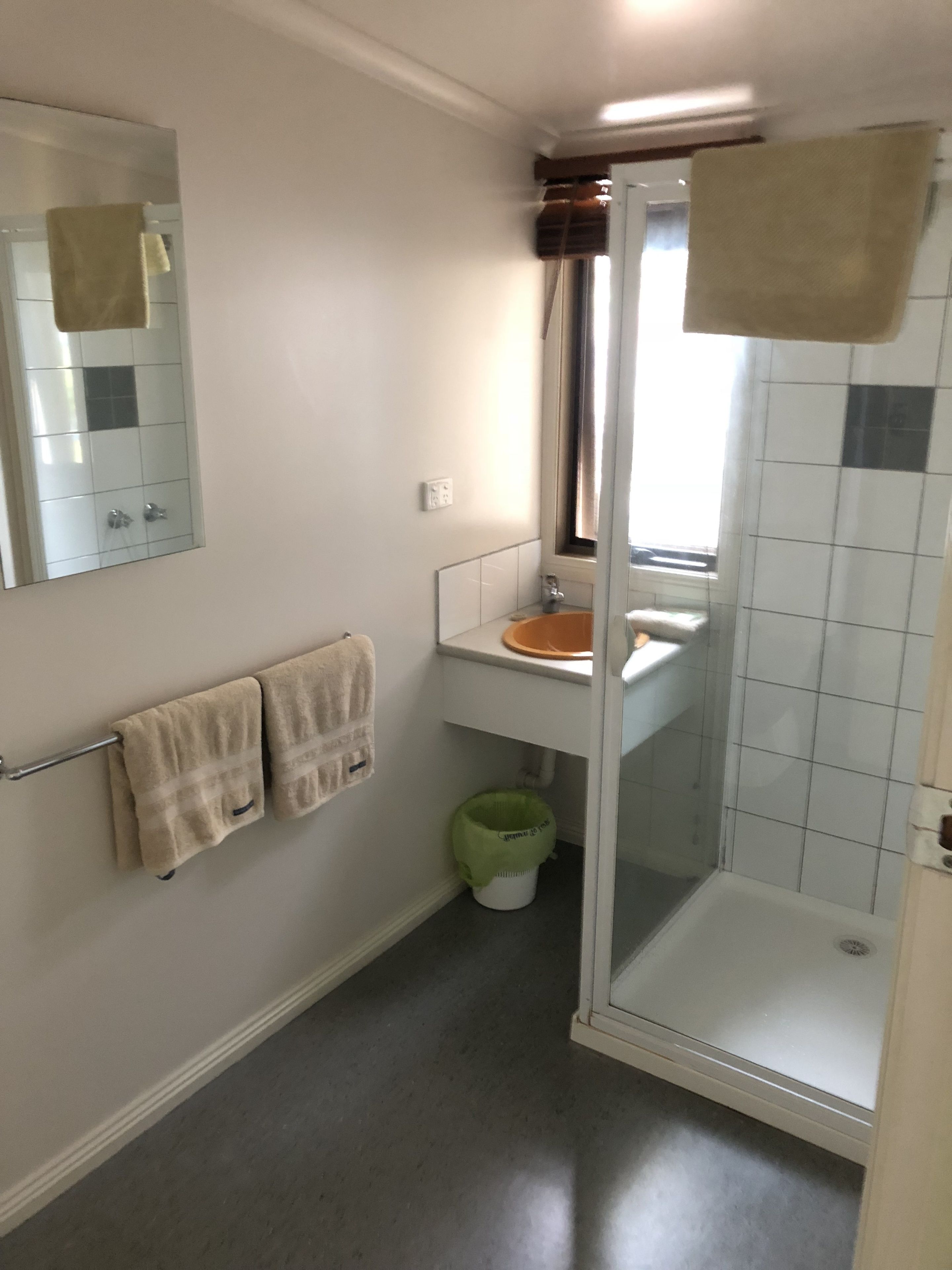 Een badkamer met een douchecabine van glas, een wastafel met een spiegel erboven en twee handdoeken aan een handdoekrek.