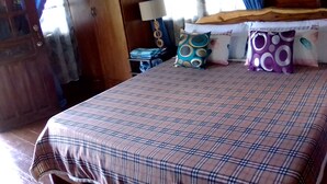 Un dormitorio con edredón de cuadros, cabecera de madera y mesita de noche con lámpara y cojines decorativos.