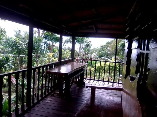 A wooden deck with a table and benches, surrounded by a railing, overlooking a lush garden.
