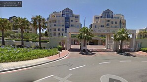 Une entrée d'hôtel moderne, avec une enseigne bien visible, des palmiers et un jardin bien entretenu.
