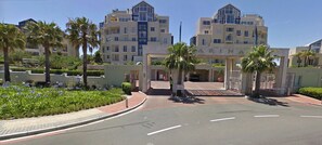 A modern hotel entrance with a prominent sign, palm trees, and a well-maintained garden.