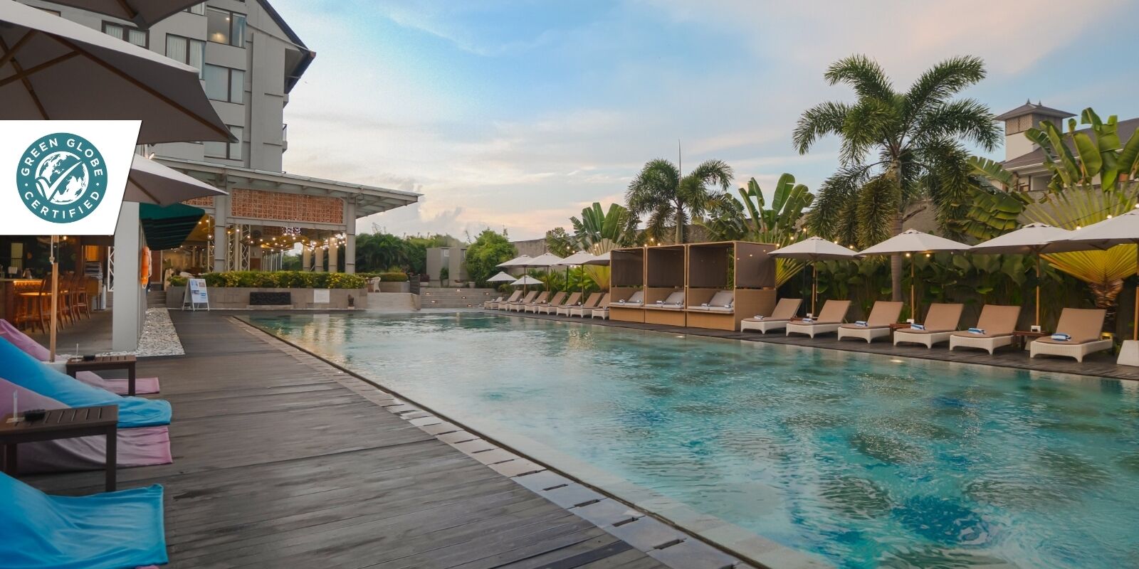 A hotel pool area with lounge chairs and umbrellas, a wooden deck, and a sign indicating Green Globe certification.