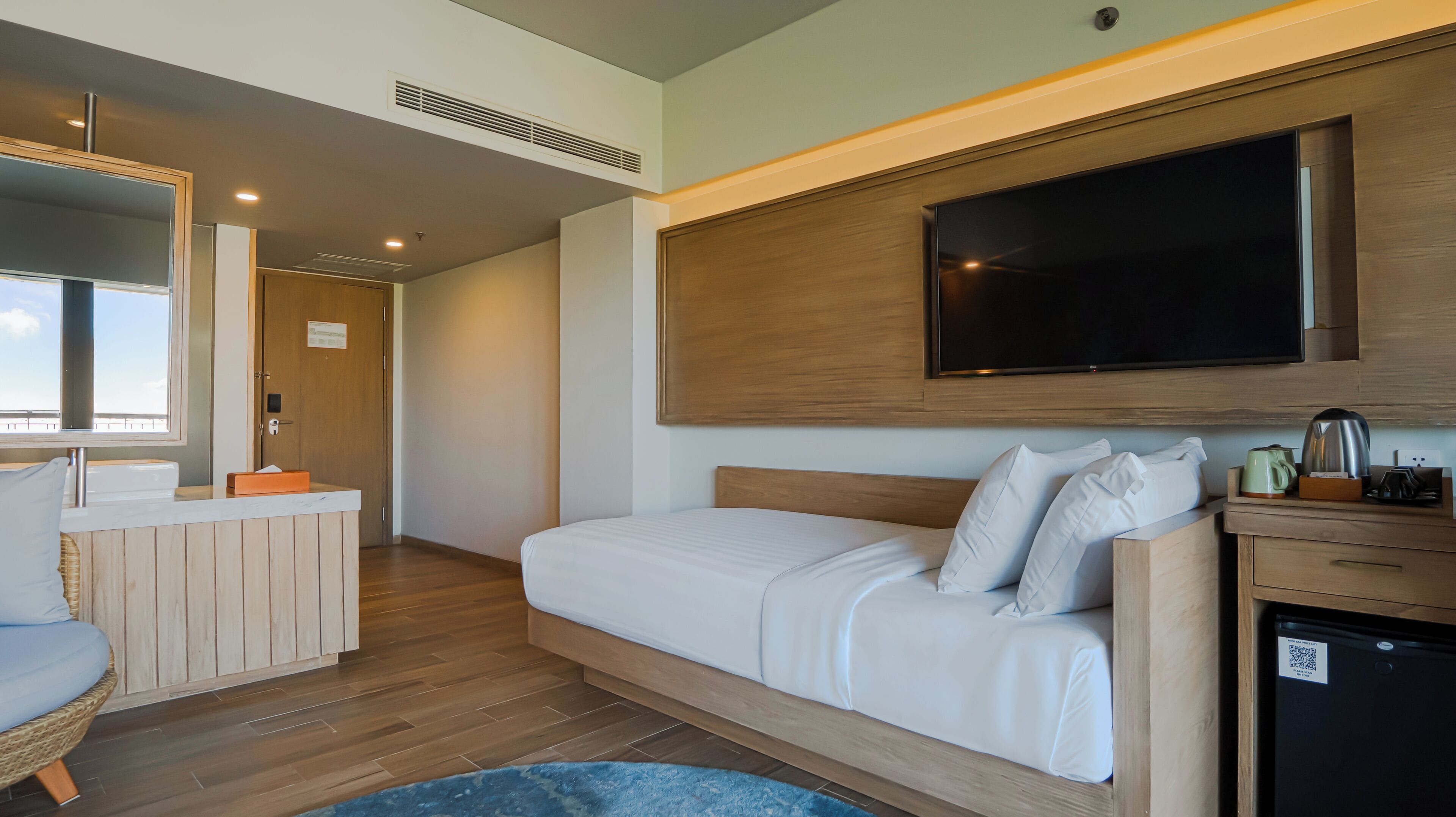 A hotel room with a bed, a TV, a small kitchenette, and a bathroom.