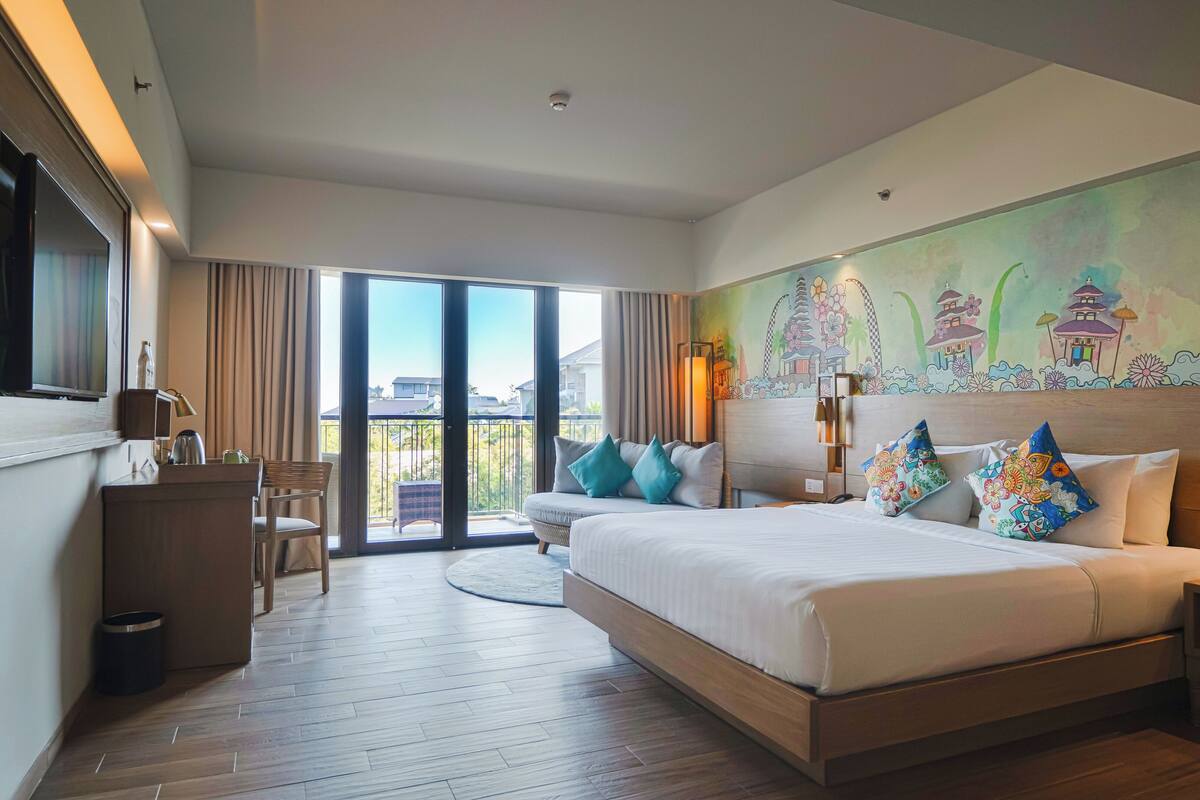 A hotel room with a large bed, a desk, a chair, and a view of the outside.