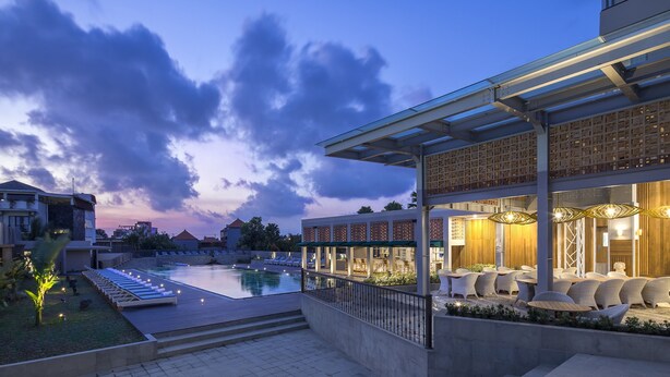A modern hotel with a pool, outdoor seating, and a covered area with lighting.