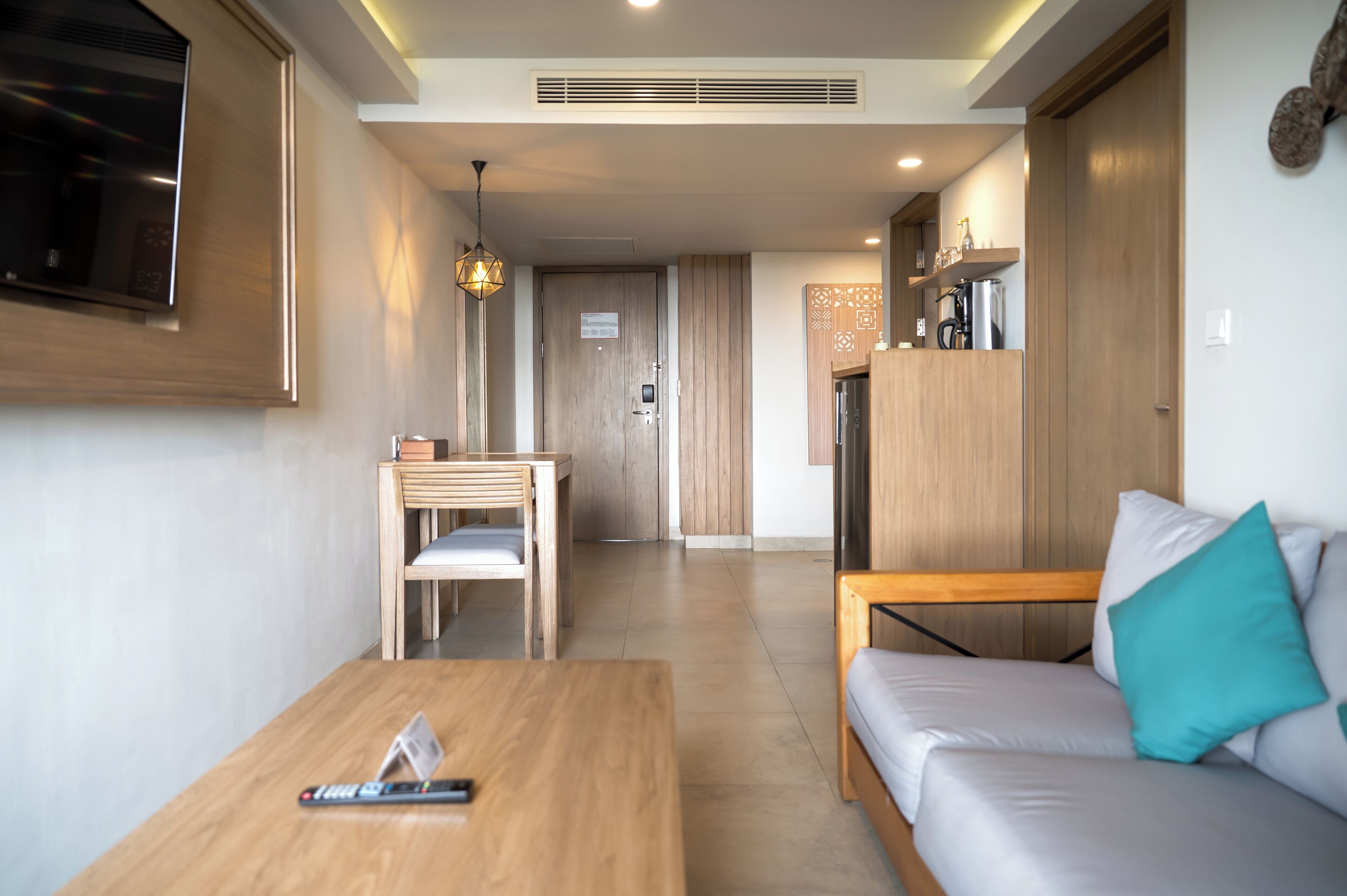 A modern hotel room with a wooden sofa, a wooden table, a TV, and a kitchenette area.