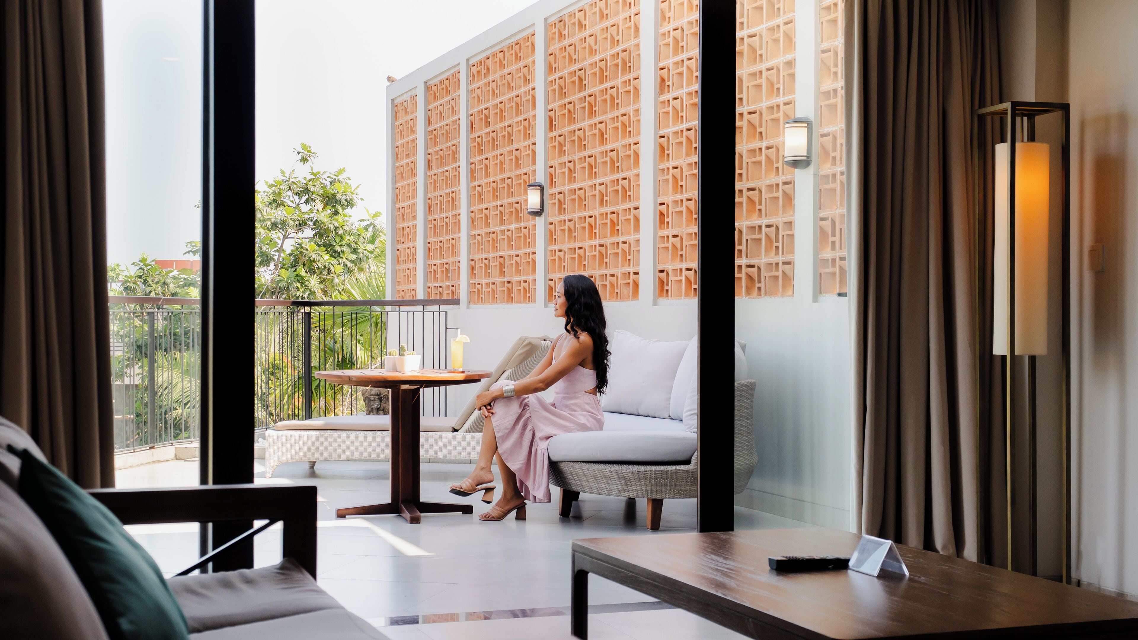 A woman sitting on a sofa in a modern room with a large window, a small table, and a wall with a geometric pattern.