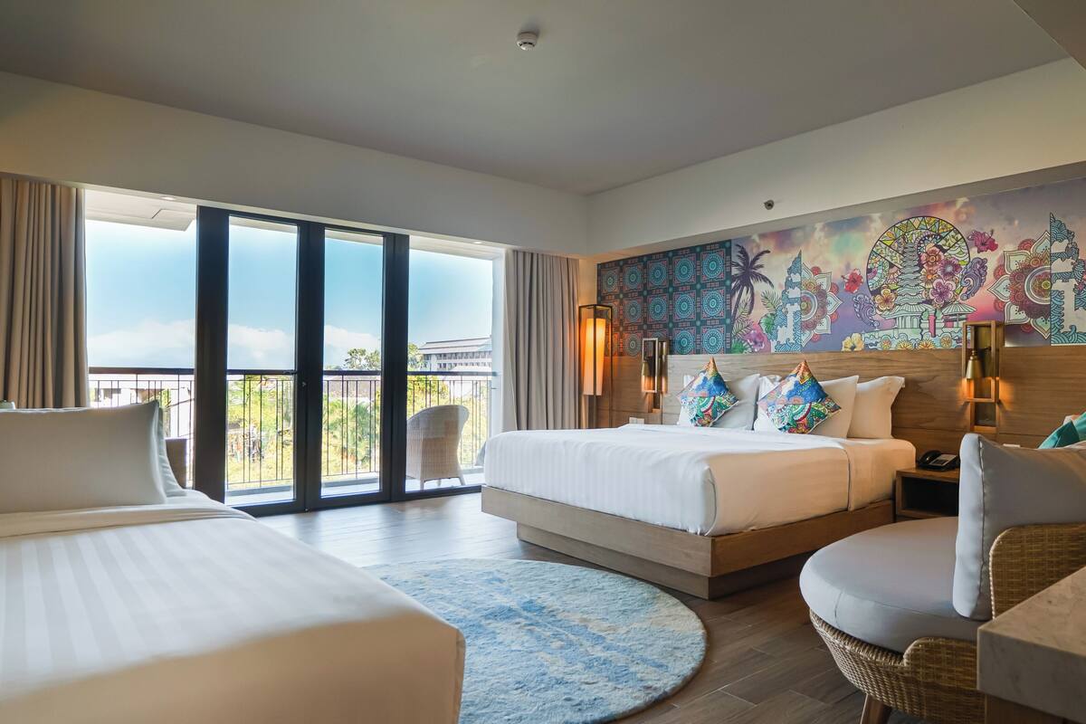 A hotel room with two beds, a balcony, a large mural, and a view of the outdoors.