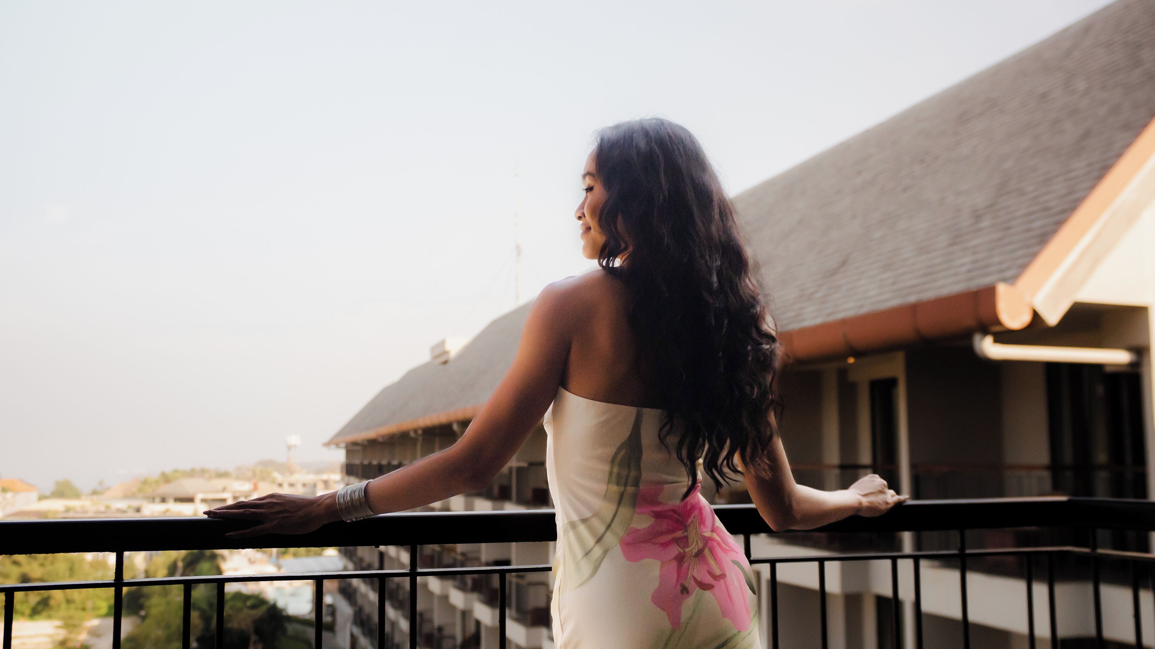 A person standing on a balcony with a railing, overlooking a building with a sloped roof.