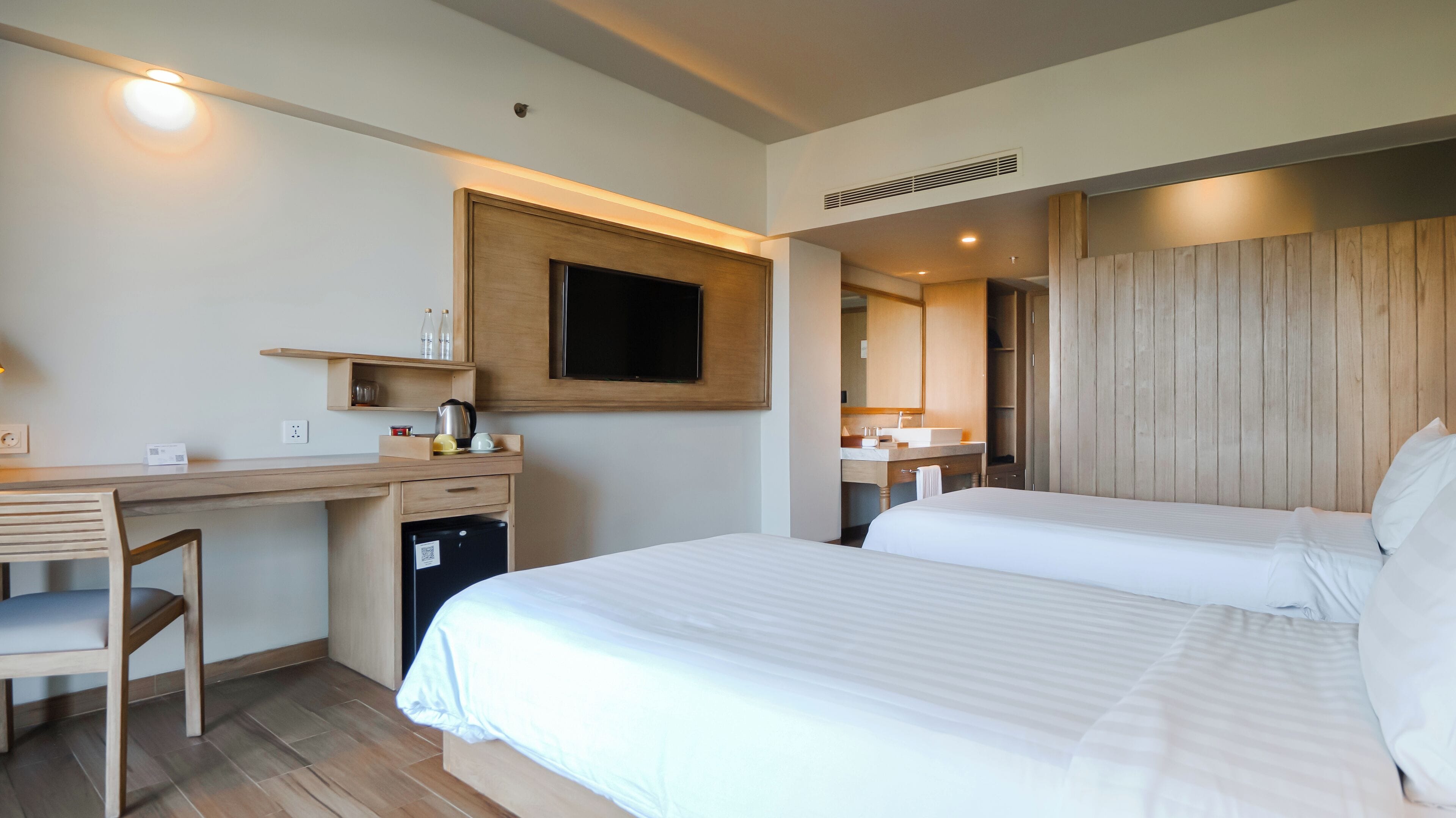 A hotel room with a bed, a desk, a chair, a TV, and a bathroom visible through an open door.