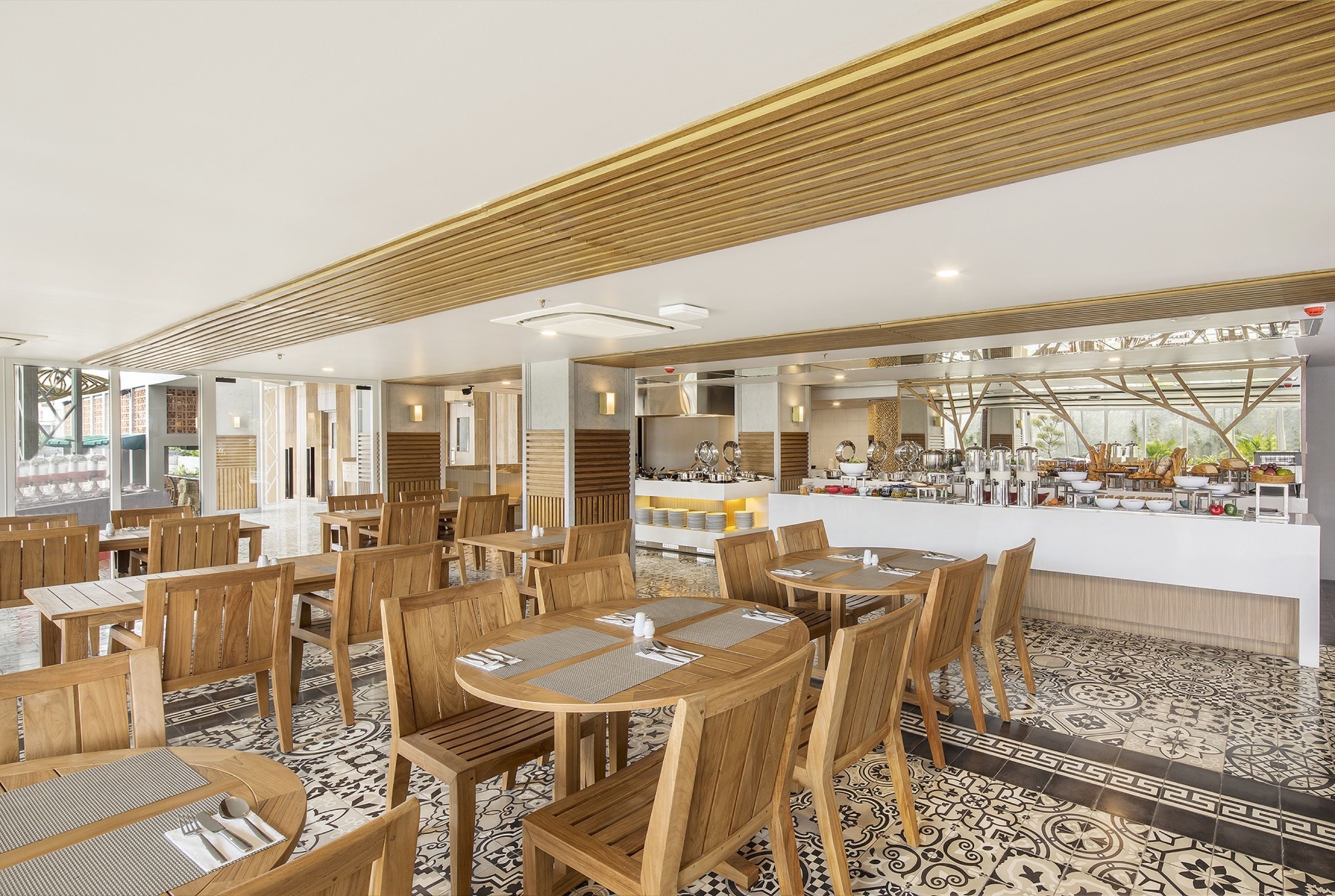 Un restaurante espacioso con mesas y sillas de madera, una zona de bar central y un suelo estampado.