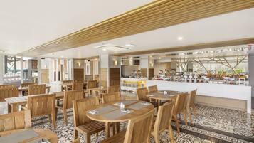 Un restaurante espacioso con mesas y sillas de madera, una zona de bar central y un suelo estampado.