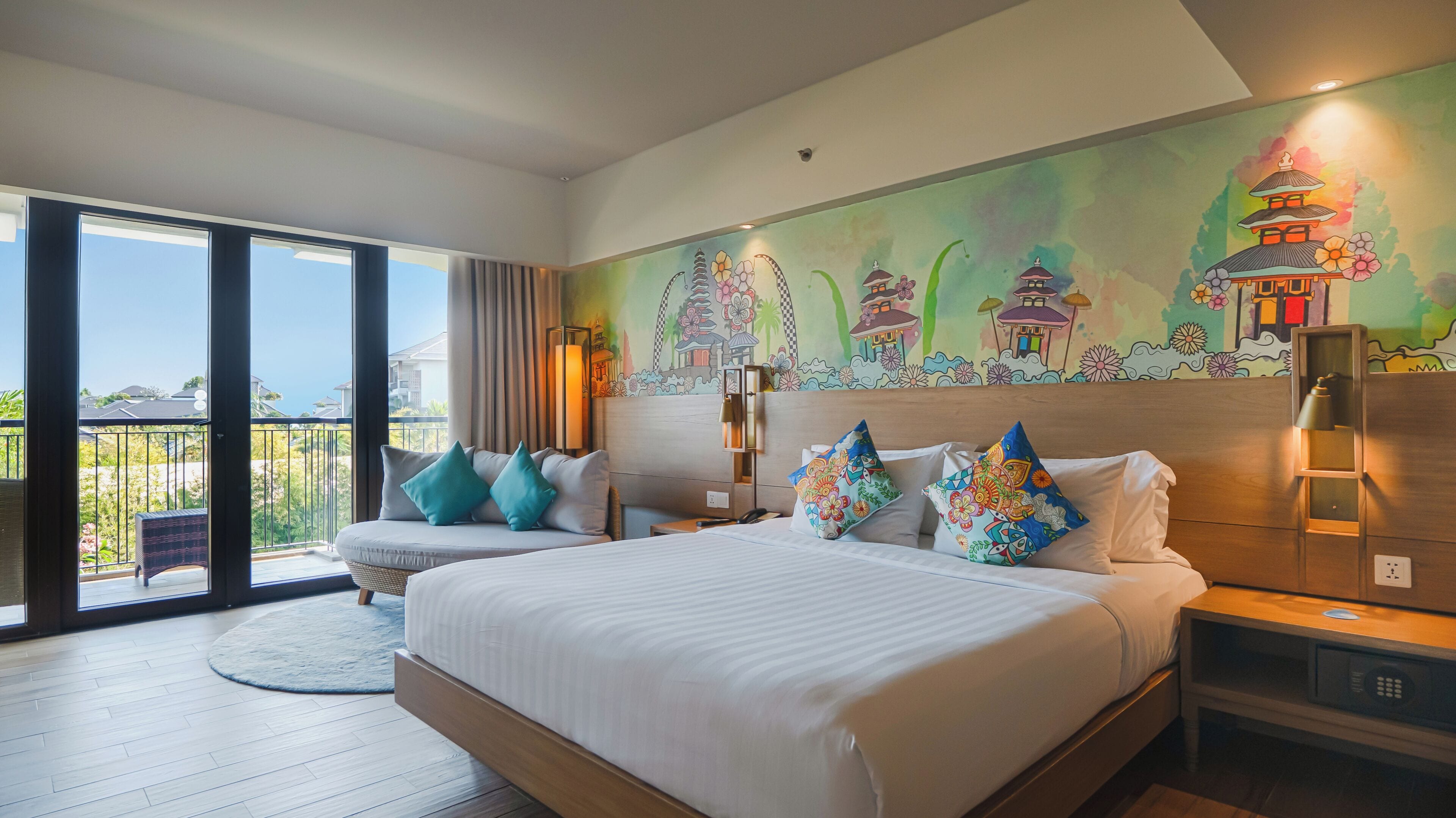 A hotel room with a large bed, a view of the sea, and a colorful mural on the wall.