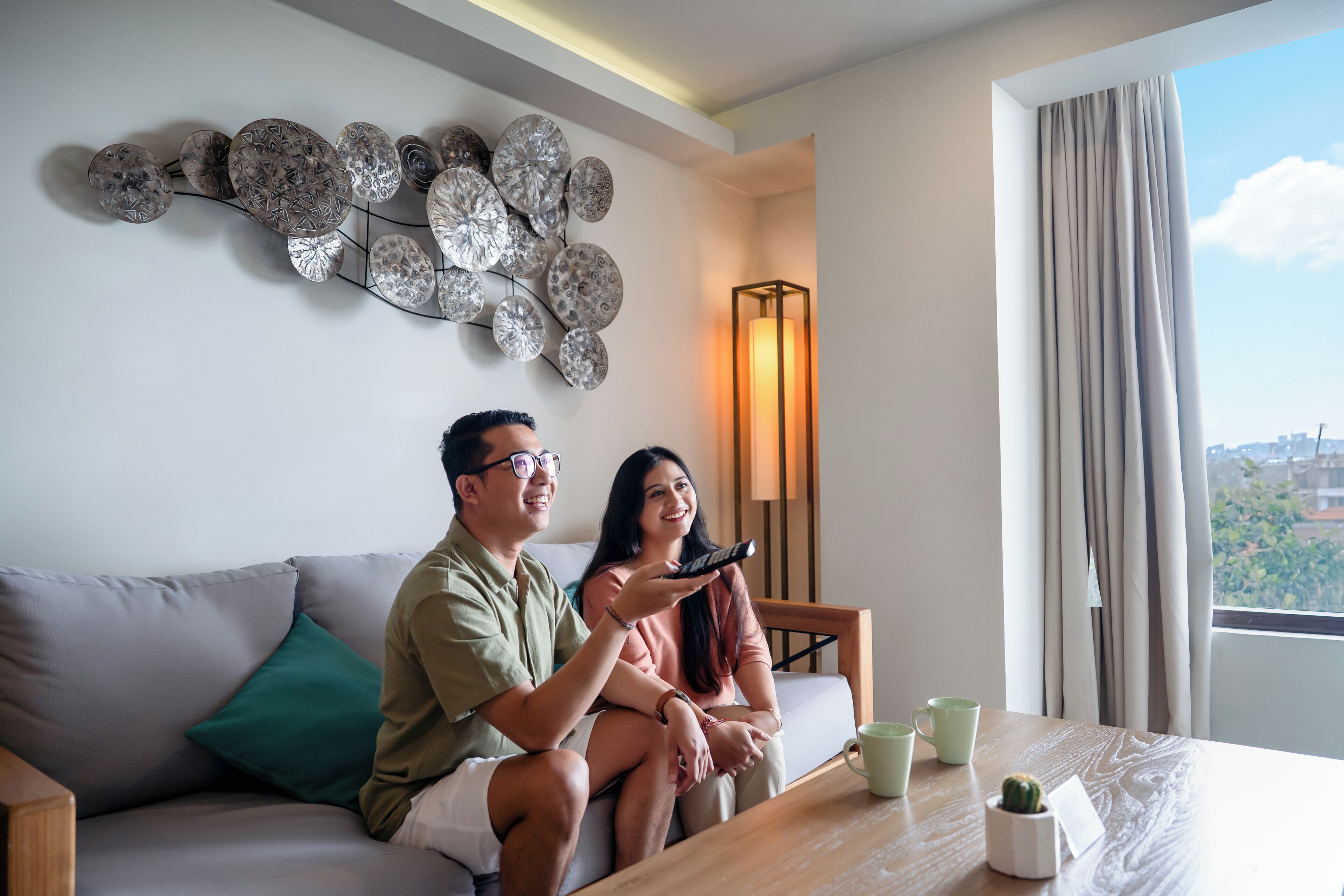 Una sala de estar moderna con un sofá, una mesa de centro con tazas y un cactus, además de un elemento decorativo en la pared.