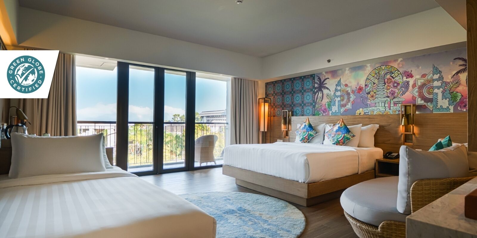 Habitación de hotel con dos camas, un balcón con vistas, un mural grande y un letrero que dice 'Green Globe Certified'.