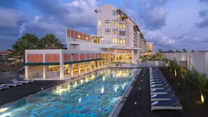 A modern hotel with a swimming pool, lounge chairs, and a well-lit exterior.