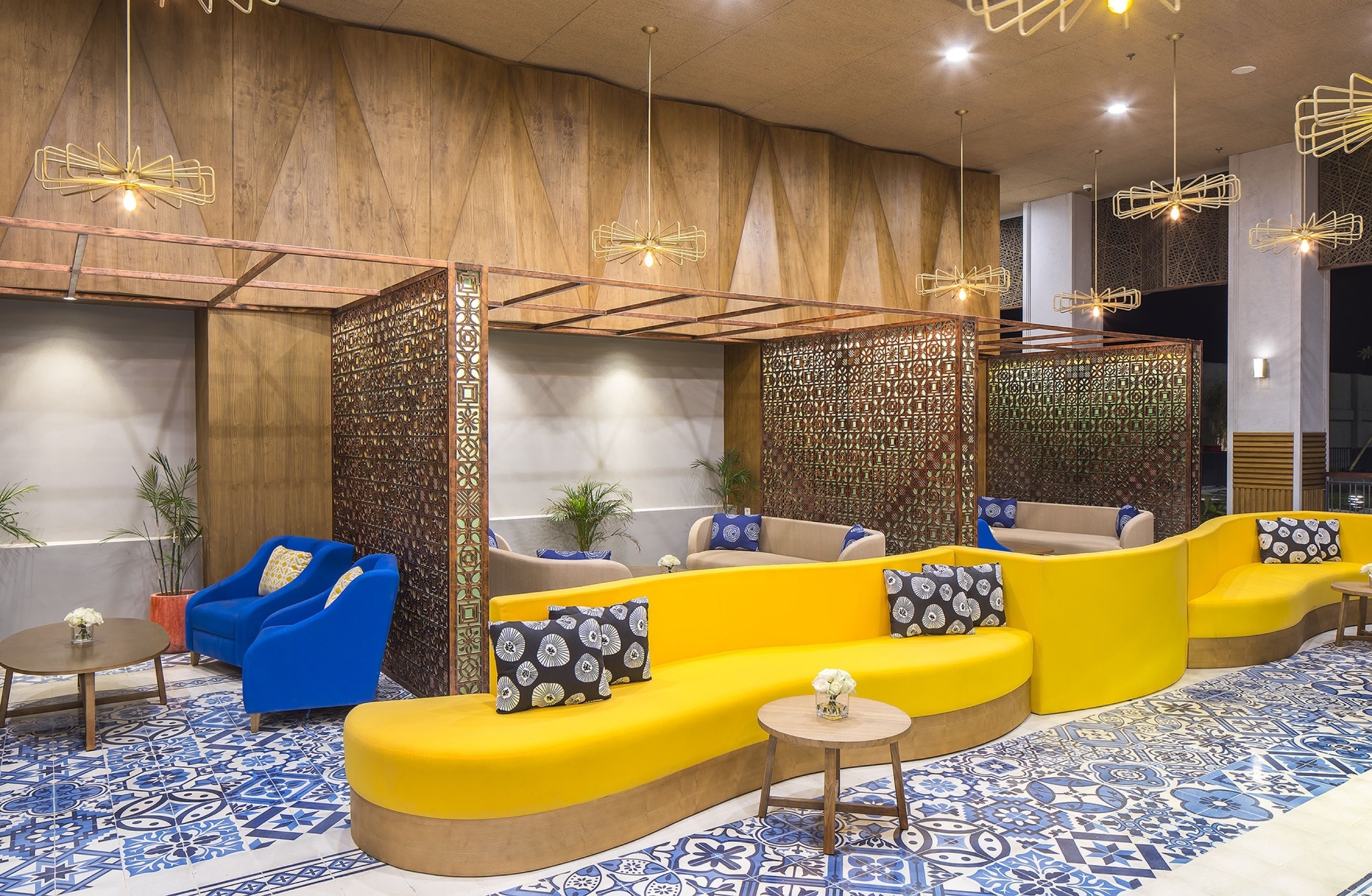A modern lounge area with yellow sofas, blue armchairs, and patterned floor tiles.
