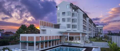 A modern hotel with a rooftop pool, multiple balconies, and a garden area.