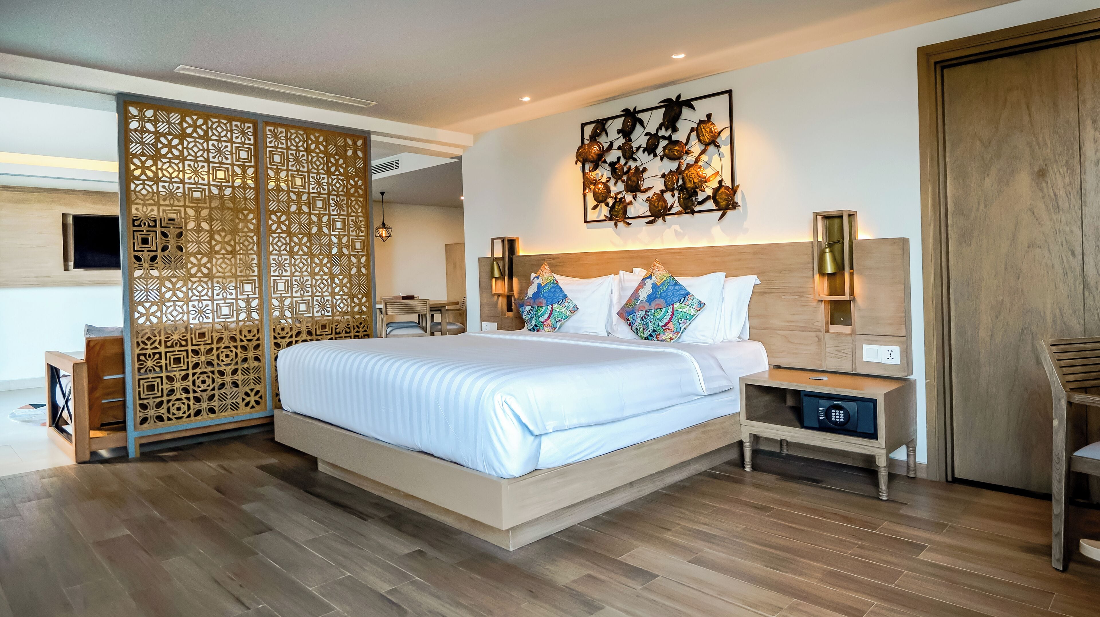A modern hotel room with a large bed, wooden floor, decorative wall art, and a wooden partition.