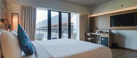 A hotel room with a large bed, a desk, a television, and a balcony with a view of buildings.