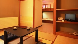 A traditional Japanese-style room with tatami flooring, a low table with a cup and a book, a bunk bed with a TV, and a telephone on a shelf. - Chalet Christiania (Yamanouchi)
