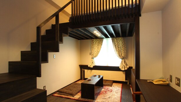 A modern interior with a wooden staircase, a small seating area with a rug, and a window with curtains. - Chalet Christiania (Yamanouchi)
