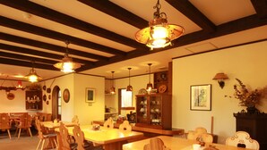 A dining area with wooden tables and chairs, hanging pendant lights, and a wooden cabinet with glass doors. - Chalet Christiania (Yamanouchi)