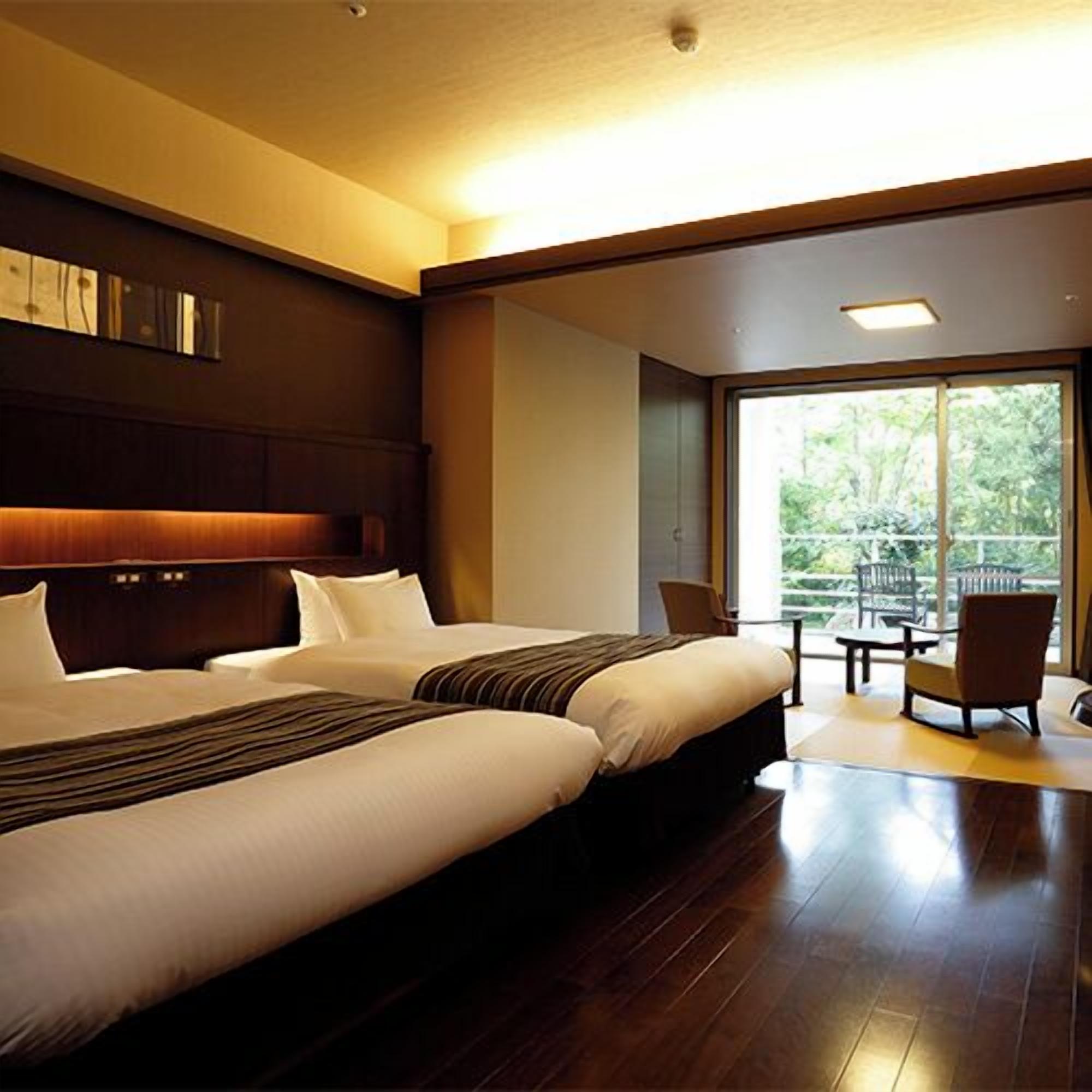 Een hotelkamer met twee bedden, een groot raam en uitzicht op groen.