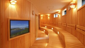 A wooden interior with a curved bench seating area, a mounted television displaying a scenic view, and wall-mounted lighting fixtures. - Hotel WELLSEASON Hamanako (Hamamatsu)