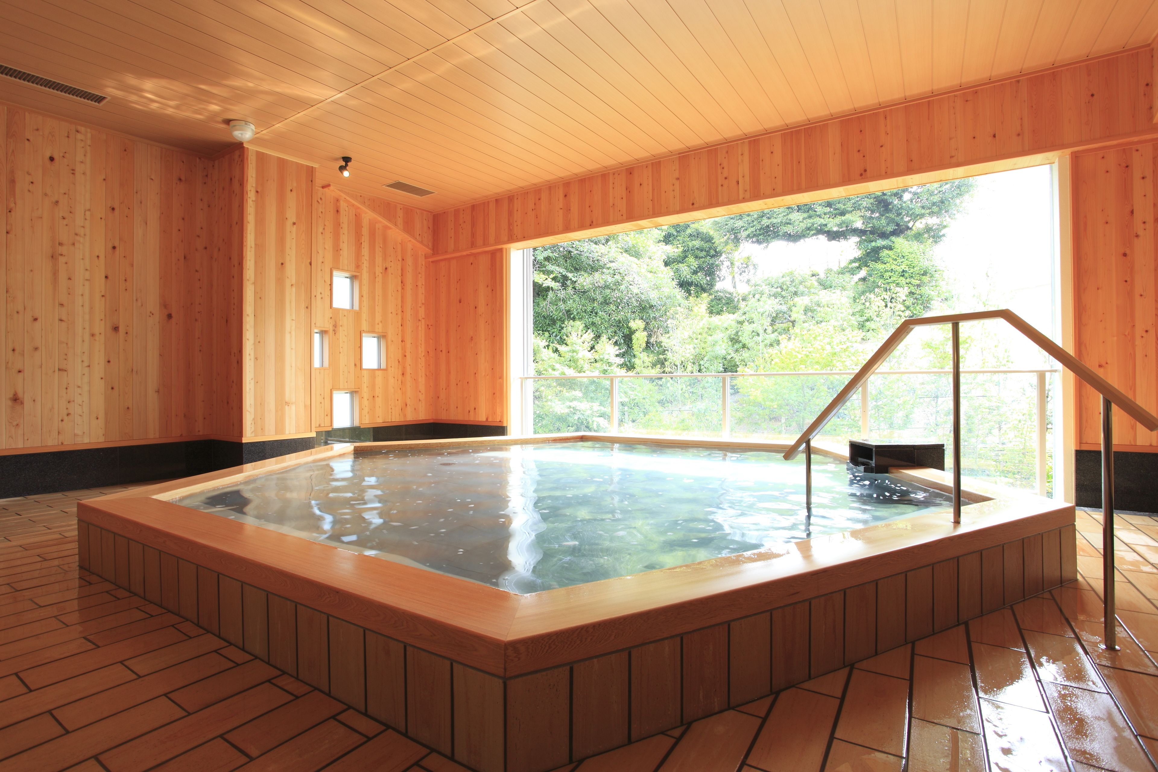 Ett spa-rum i trä med ett bubbelbad, träväggar och ett stort fönster med utsikt över grönskan.
