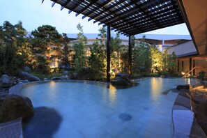 A serene outdoor pool area with a wooden pergola, surrounded by rocks and trees, and a building in the background. - Hotel WELLSEASON Hamanako (Hamamatsu)