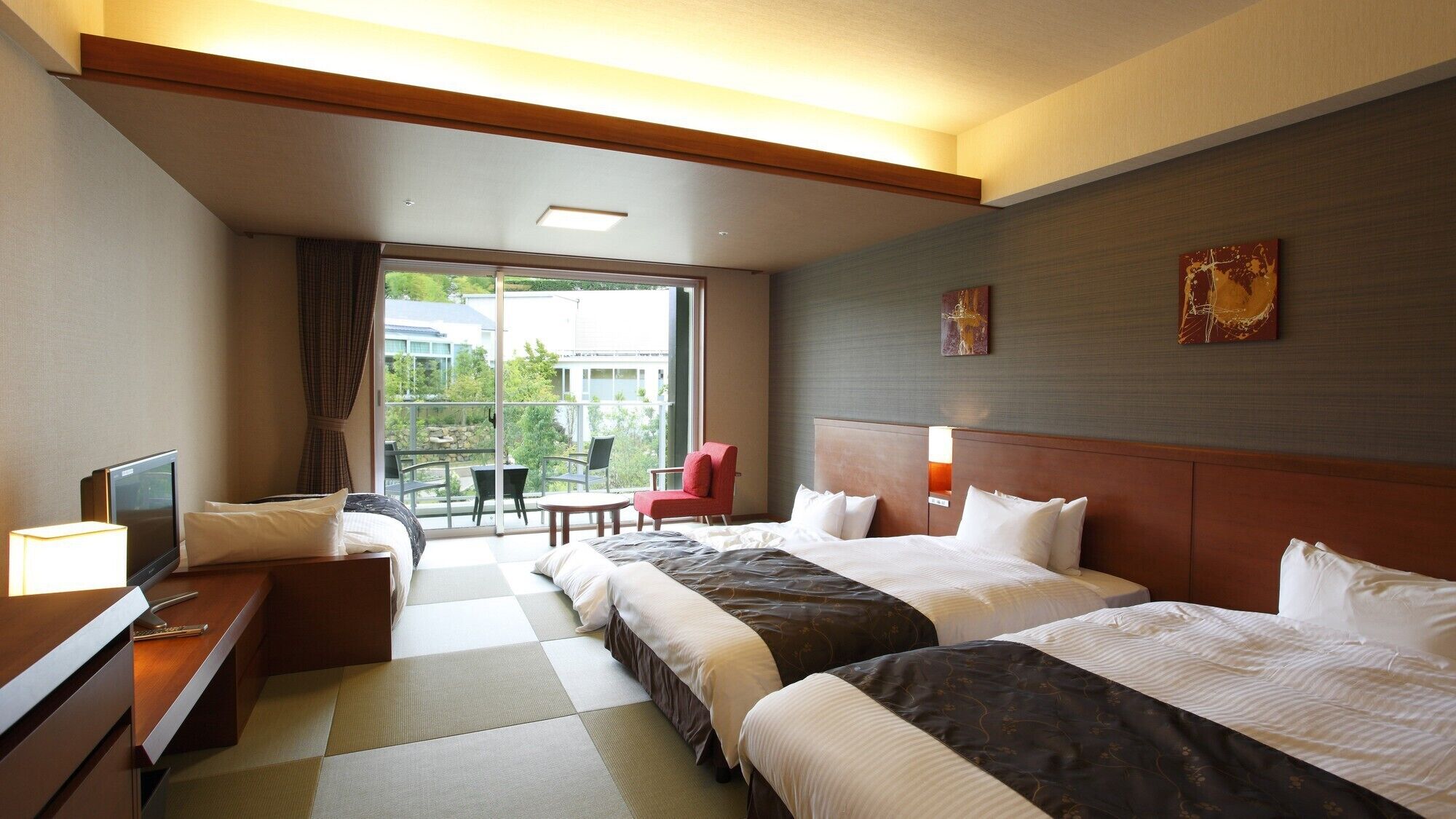 Een hotelkamer met twee bedden, een bureau, een televisie, een balkon met een tafel en stoelen, en kunstwerken aan de wanden.