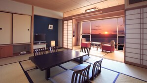 A traditional Japanese room with tatami flooring, a low table, and sliding doors leading to a balcony with a sunset view. - Hotel WELLSEASON Hamanako (Hamamatsu)