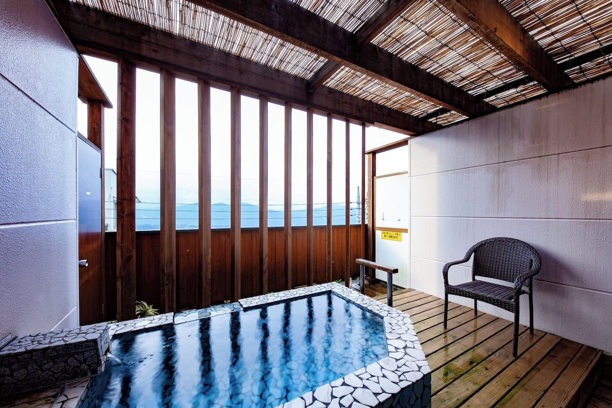 A hot tub area with a wooden deck, a chair, and a view of the sea.