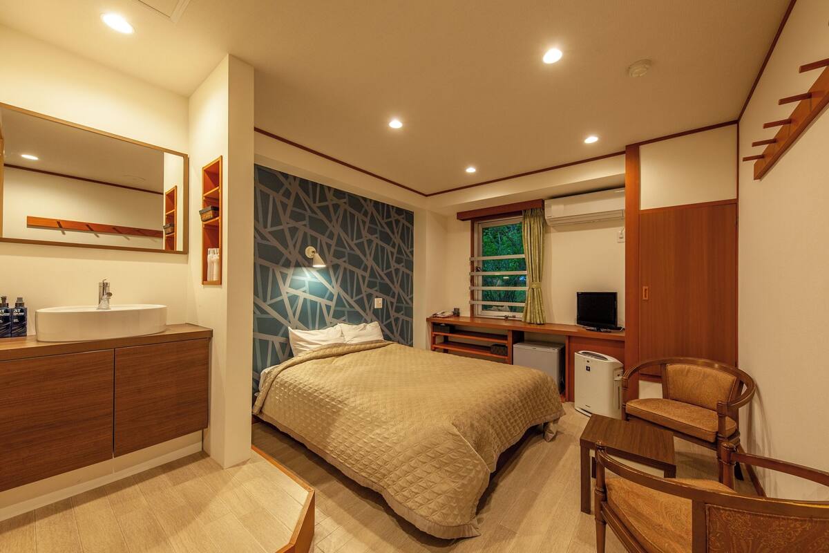Une chambre d’hôtel moderne avec un grand lit, une table de chevet, un bureau avec une chaise, un miroir et une télévision.