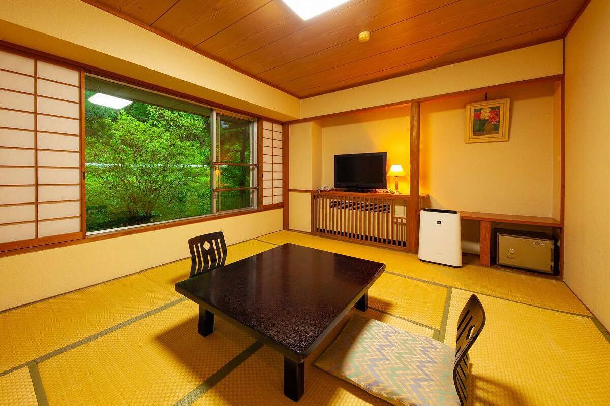 Une pièce de style japonais traditionnel, avec un sol recouvert de tatamis, une table basse, des chaises, un téléviseur et un radiateur.