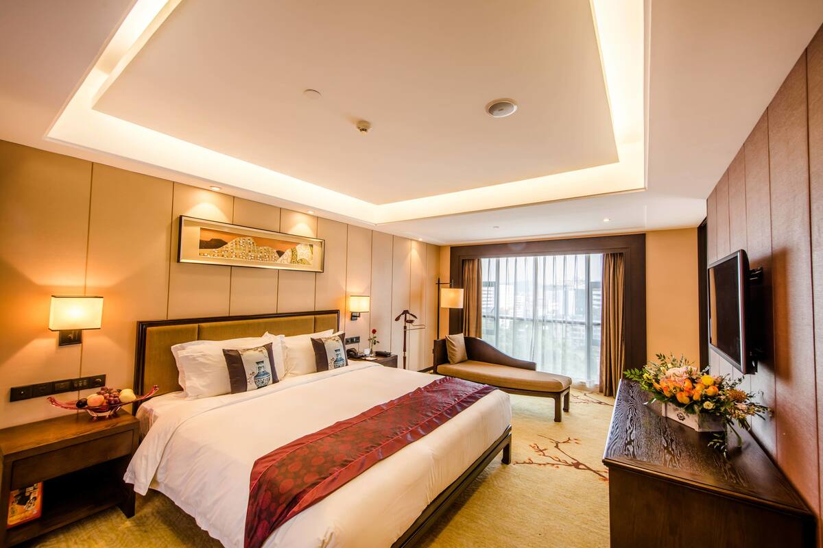 Une chambre d’hôtel avec un grand lit, des tables de chevet, un bureau, une chaise, une télévision et une fenêtre avec des rideaux.